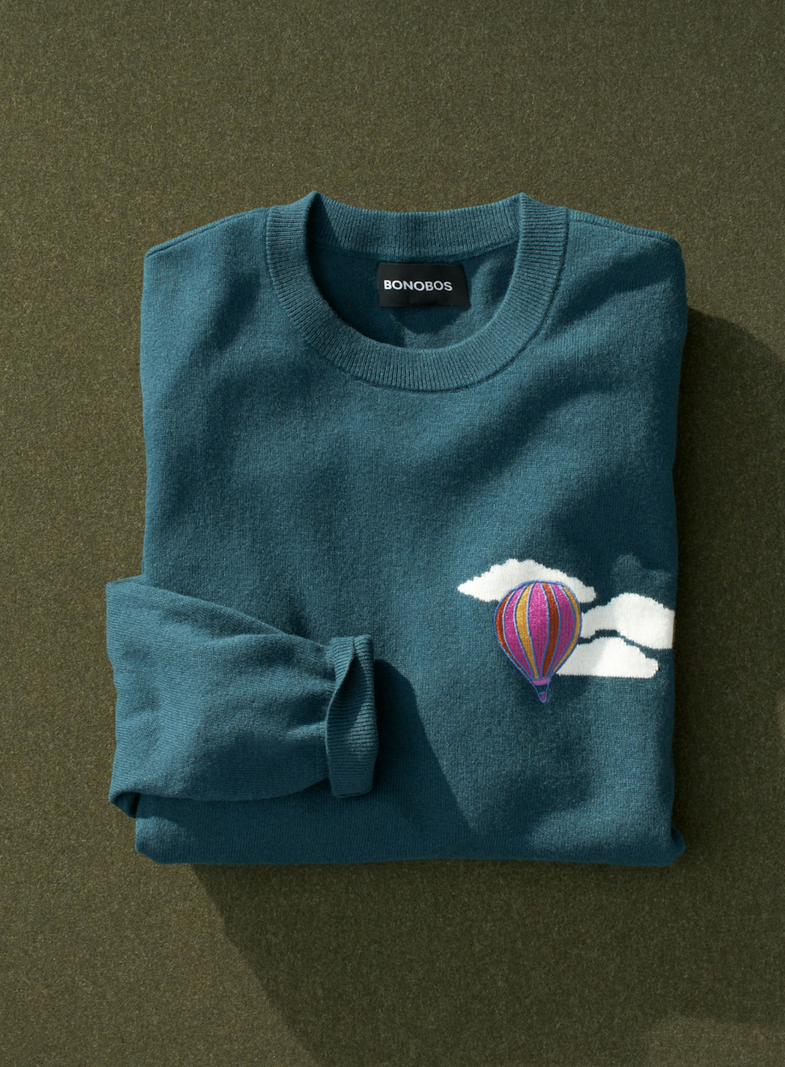 image of folded limited edition Sweater, teal sweater with clouds and hot air balloon. 