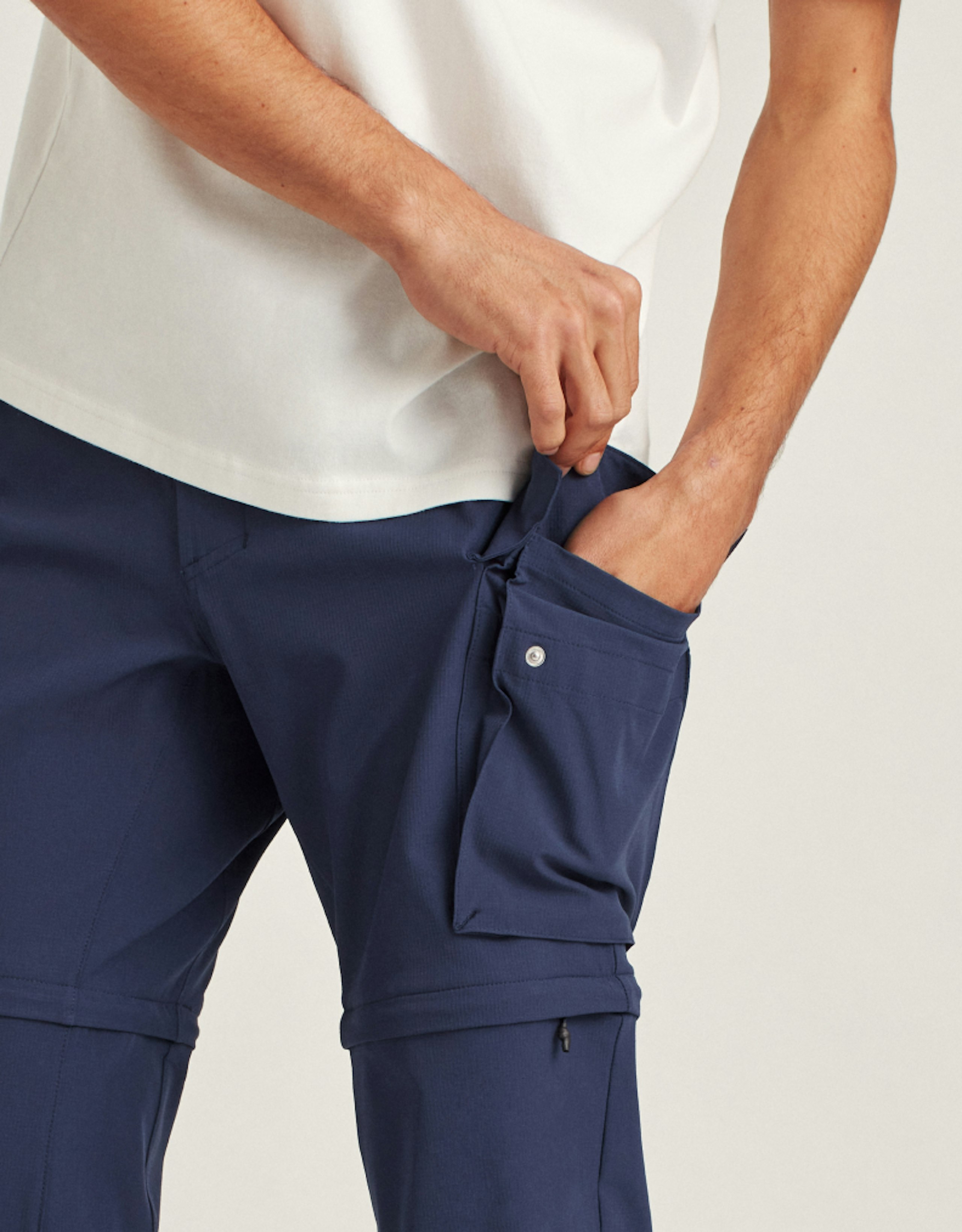 Man in blue Stretch Convertible Cargo Pant demonstrating functionality of pocket by putting hand in pocket.