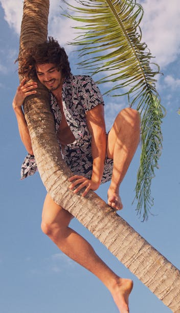 model climbing palm tree wearing Easy Lightweight Shorts and Riviera Cabana Shirt in Black Trippy Floral
