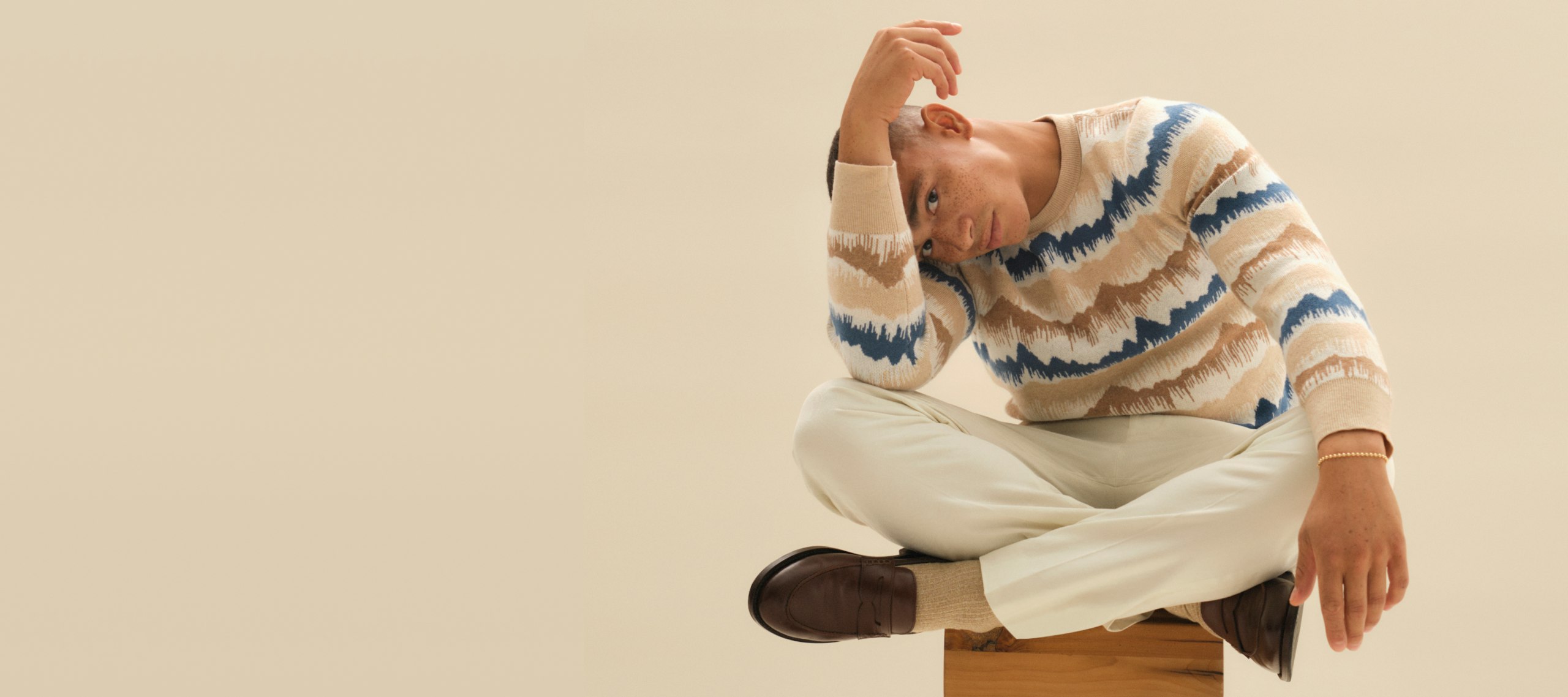 Model sitting cross legged wearing Mountain Blur Limited Edition Sweater and Vanilla Stretch Italian Chinos