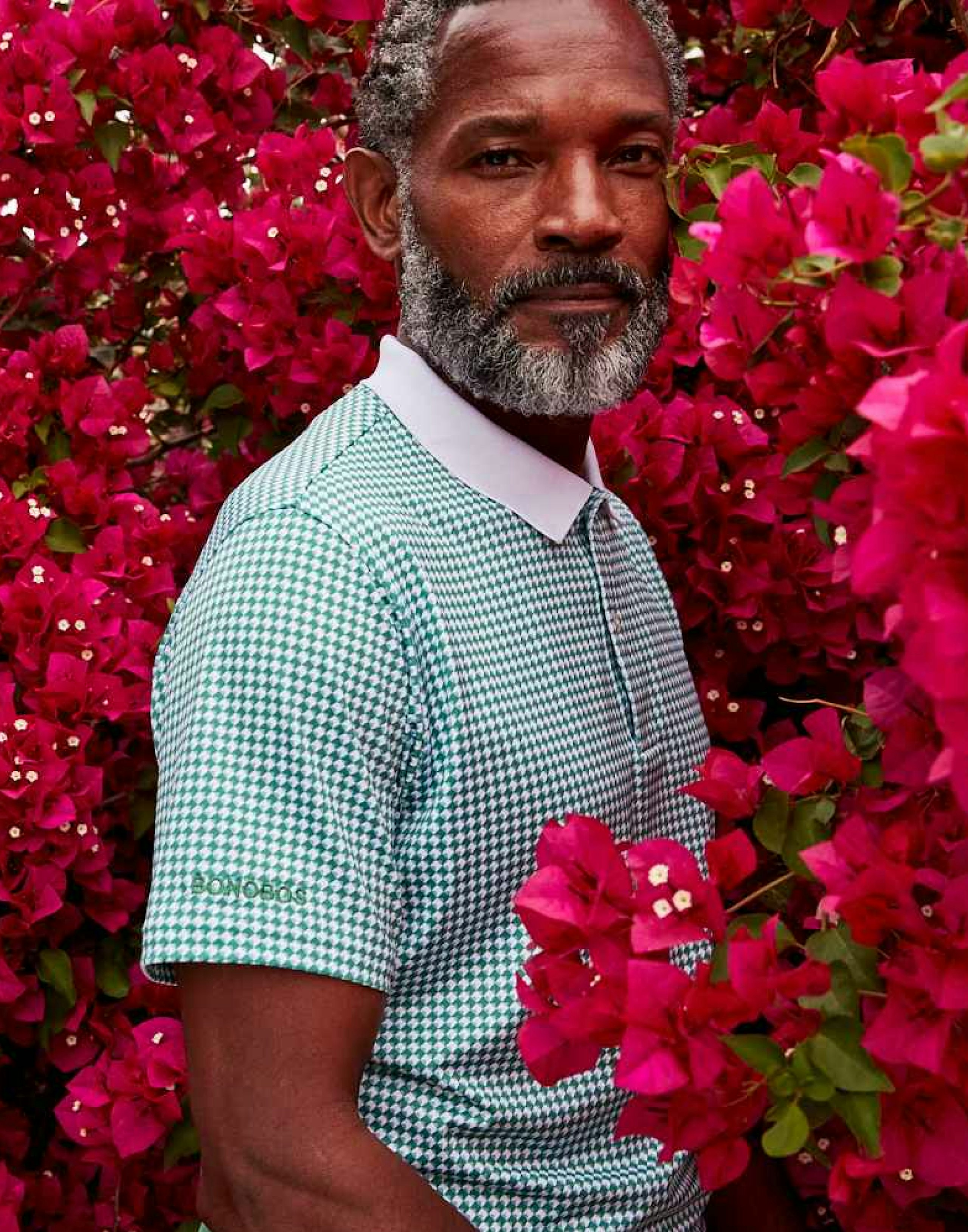 Person facing camera straight on wearing a golf polo standing surrounded by flowers