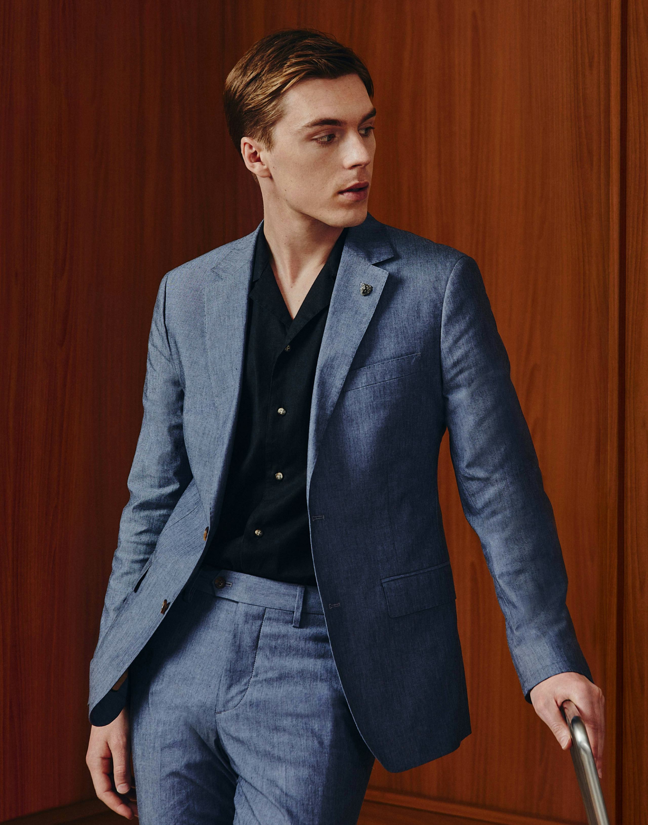 Model wearing Portuguese Stretch Chambray Suit and riviera cabana shirt in front of wooden panels