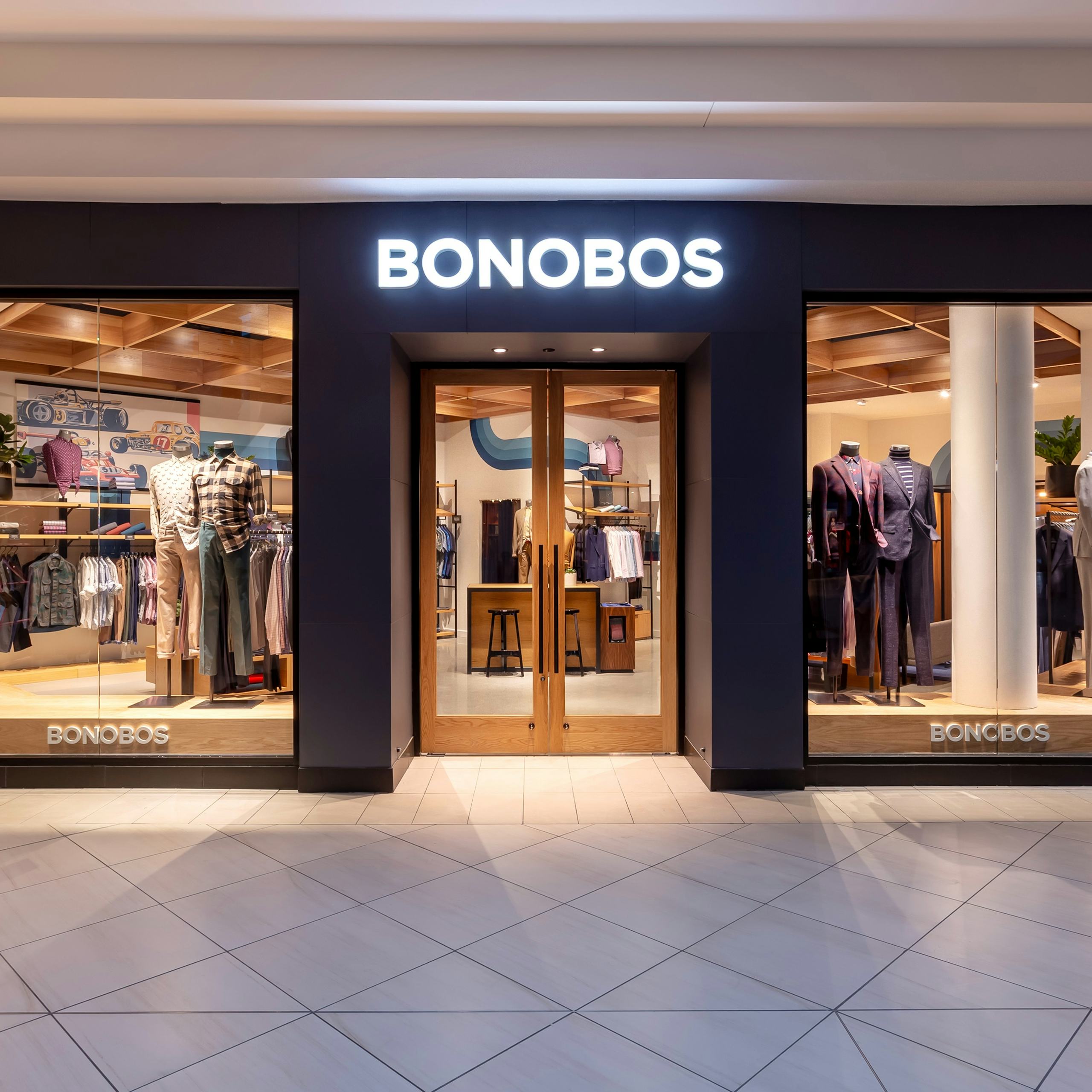 Image of Bonobos Store in The Fashion Mall At Keystone Crossing, Indianapolis. There are 2 mannequins with suits on the right side, and 2 mannequins with casual shirts and chinos and on the left side.  